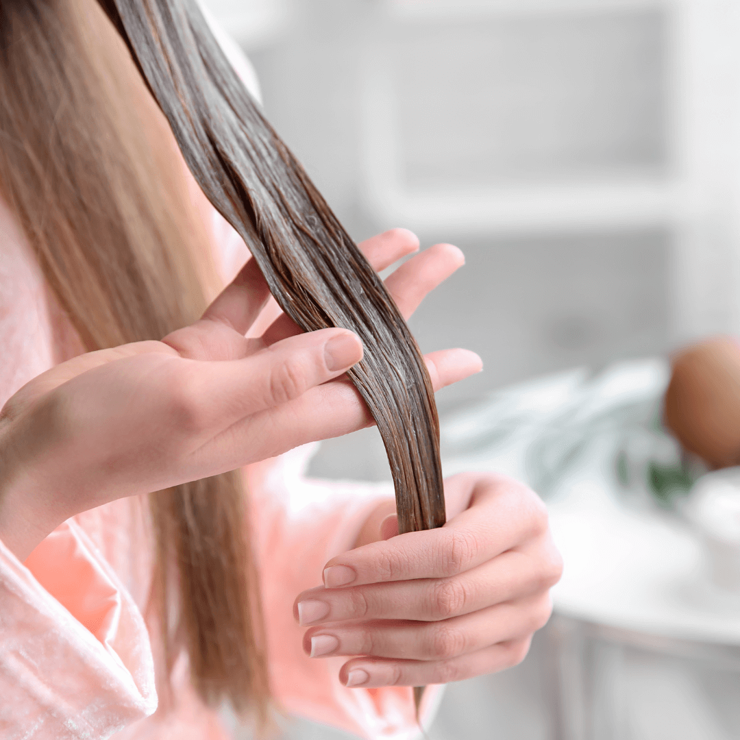 una persona tomando su cabello y mostrando que aplico mascarilla capilar en un mechón